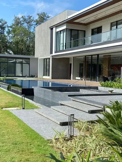 The expansive view of a modern Delhi farmhouse, where a pristine swimming pool and manicured lawn meet contemporary architecture. This project showcases our ability to create seamless transitions between indoor comfort and outdoor splendor, featuring clean lines and lush greenery.