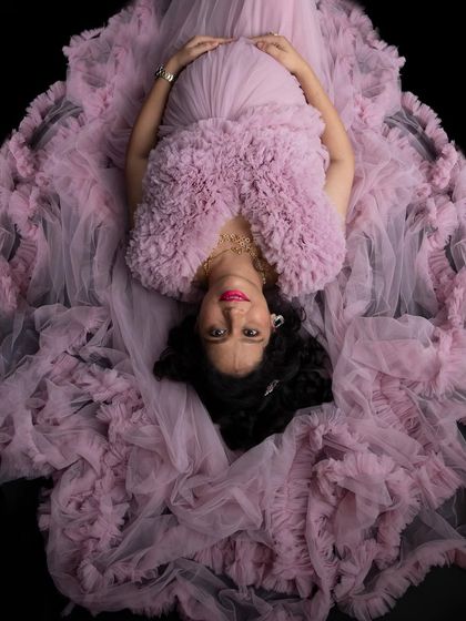 A glamorous overhead shot. The mom-to-be looks stunning, nestled in a bed of lavender ruffles against a stark black background.