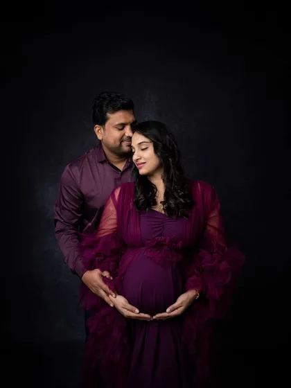 A quiet and intimate pose where the couple gently holds the baby bump together. The low-key lighting creates a very personal and heartfelt mood.