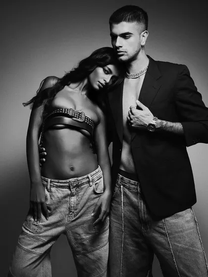 A modern and edgy couple's portrait in black and white. The styling, with denim and a leather harness top, creates a bold look, while the pose conveys a sense of relaxed intimacy and confidence.