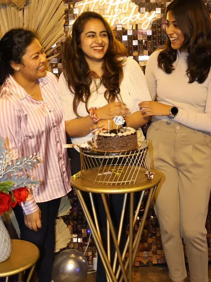 Laughter and smiles during a cake-cutting ceremony. This candid shot captures the pure joy of friends celebrating a birthday together against our shimmering sequin wall.