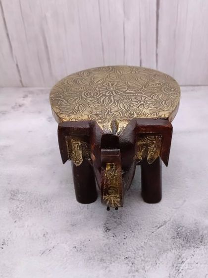 A wooden bajoth or chowki in the shape of an elephant with a brass top. This elegant stool is used to place idols.