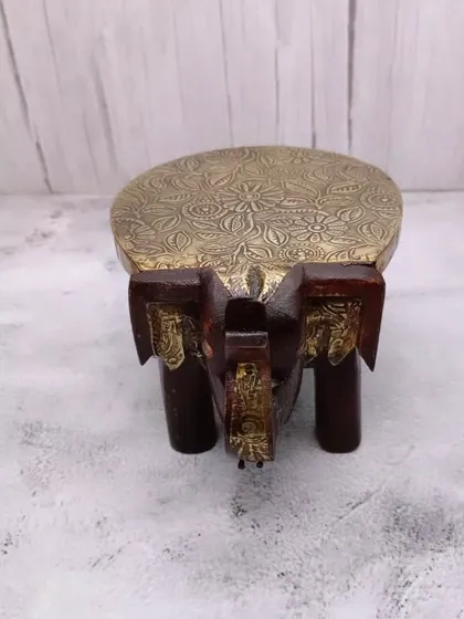 A top-down view of the wooden elephant chowki, showing the detailed floral embossing on the brass surface.