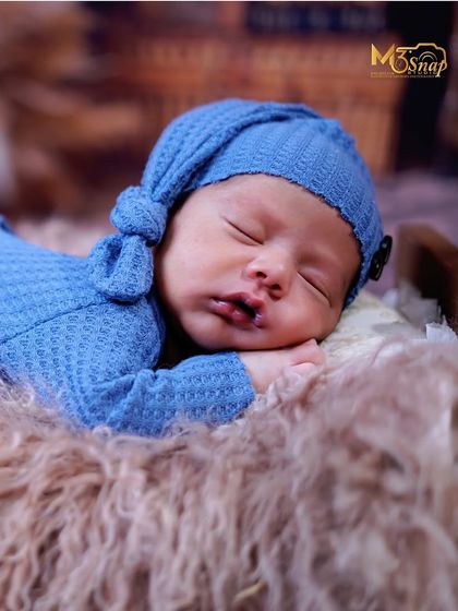 A close-up portrait of a sleeping newborn in a blue knotted hat. The focus here is on their sweet, peaceful face and tiny features.
