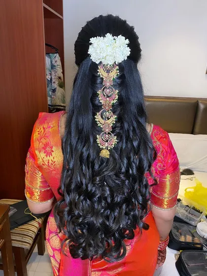 A unique half-updo with open curls, adorned with a traditional jasmine gajra and a central piece of temple jewellery.