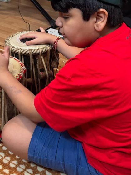 A close-up of a young student learning the tabla. He is focused on the intricate hand movements required to produce the instrument's wide range of sounds.