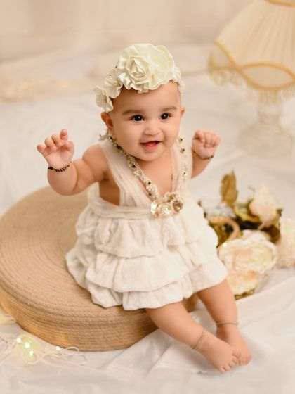 A happy baby in a beautiful vintage-style dress, ready to clap her hands. The warm, soft lighting creates a dreamy and gentle mood.