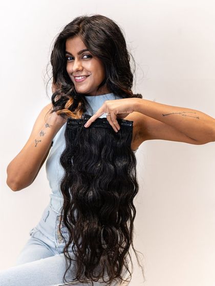 A happy model showing off her wavy hair, holding a matching clip-in set. Our extensions are perfect for enhancing your natural texture and adding glamorous volume.