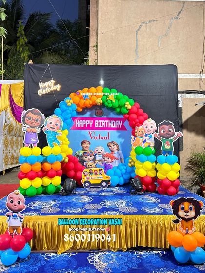 A Cocomelon stage setup for Vatsal's first birthday. This outdoor decoration includes a custom backdrop, a colorful balloon arch, and multiple character cutouts.