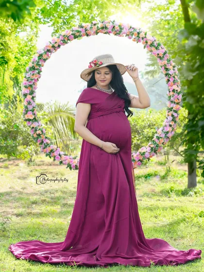 A serene portrait of a mother-to-be in a wine-colored gown and hat, framed by a circular floral prop.