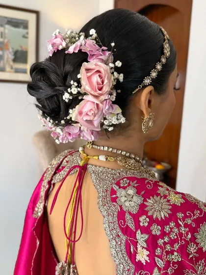A close-up of a low bridal bun decorated with fresh pink roses and baby's breath. The addition of a delicate matha patti completes this traditional look.