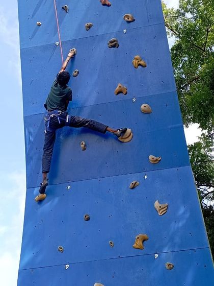 A climber stretches for a hold during a top-rope session at the Davangere climbing facility.