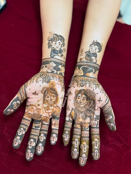 A unique baby shower mehendi featuring portraits of little Krishna and Radha on the palms, with drawings of the client's children on the forearms.