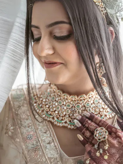 A serene close-up of a bride with her eyes closed, showcasing her beautiful makeup, intricate necklace, and the fine details of her mehendi.