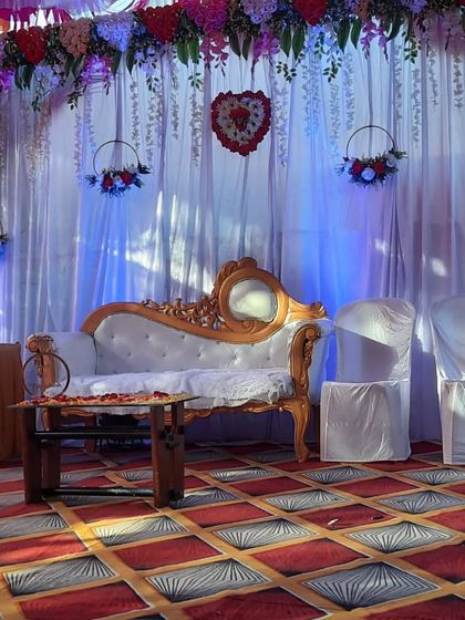 A cozy engagement setup with a white divan, side chairs, and a backdrop of white drapes with hanging floral hoops. This is great for smaller, more intimate functions.