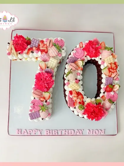 A beautiful number cake for a 70th birthday. The "70" is decorated with pink and white frosting, fresh strawberries, and chocolates.