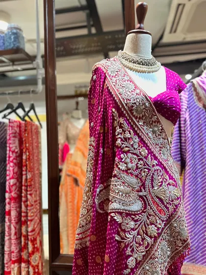 A saree is always a classic choice. This piece stands out with its heavily embroidered peacock motifs on the pallu, set against a deep magenta bandhani fabric.