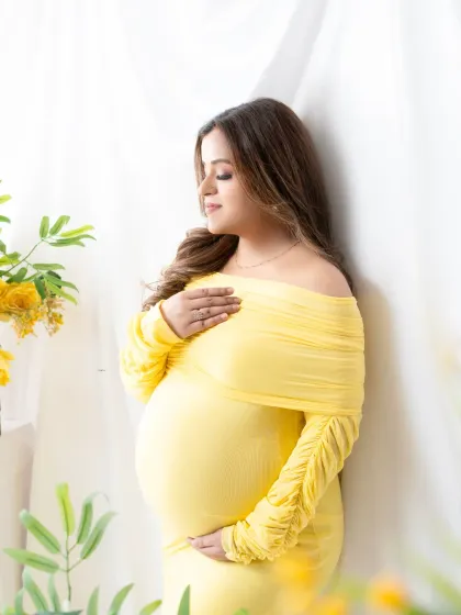 A moment of quiet connection. The mother-to-be holds her bump, her yellow off-the-shoulder gown adding a warm and cheerful glow to the portrait.