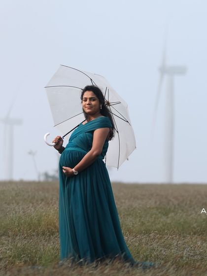 A moody and atmospheric maternity shot. The teal gown and a clear umbrella create a beautiful photo, even on a misty day with windmills in the background.