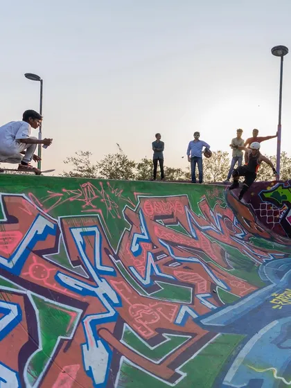 Skaters dropping into the bowl, which is now covered in vibrant graffiti from multiple artists. The art follows the curves and lines of the architecture.