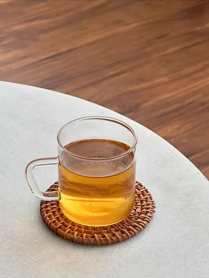 A simple, minimalist shot of a glass of tea on a wicker coaster, focusing on the warm color of the brew and the clean aesthetic of the moment.
