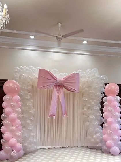 A classic and elegant balloon arch in white and clear balloons, finished with a large, structured pink bow. This is a perfect photo backdrop for baby showers or birthdays.