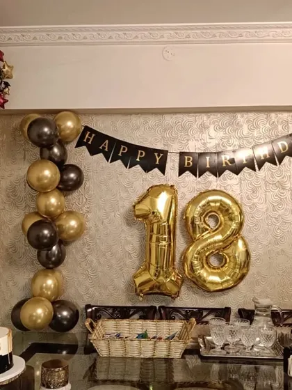An elegant 18th birthday party setup. This decoration features a black and gold theme with a 'Happy Birthday' banner, large '18' foil balloons, and coordinated balloon garlands, creating a sophisticated look for a milestone celebration.