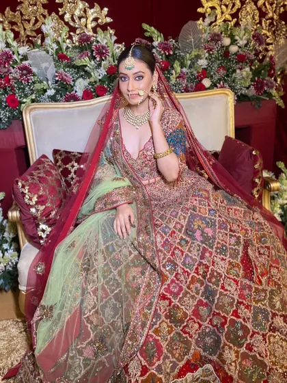 The epitome of a royal bride, seated on a throne-like chair. The multi-colored lehenga is a work of art, and the makeup is designed to be equally regal, with a flawless finish and defined features.