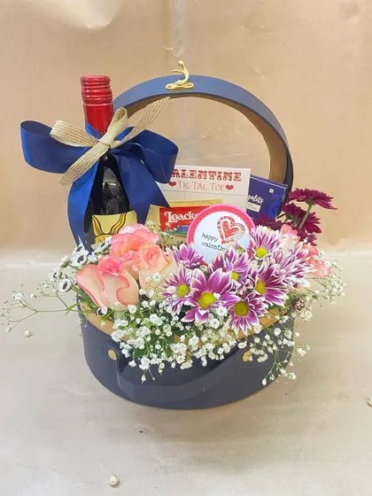 A sophisticated gift basket featuring wine, tic-tac-toe chocolates, and a fresh floral arrangement in a stylish navy blue and leatherette basket.