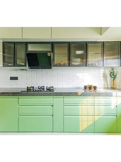Sunlight streams into this cheerful green kitchen, highlighting the clean lines and fresh color palette. The fluted glass on the overhead cabinets adds a touch of texture.