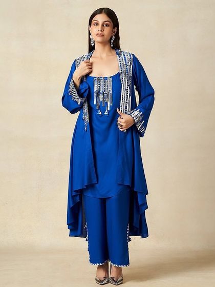 A full-length shot showcasing a modern ethnic look. The makeup is clean with a soft smokey eye, paired with simple hair to complement the layered blue outfit.