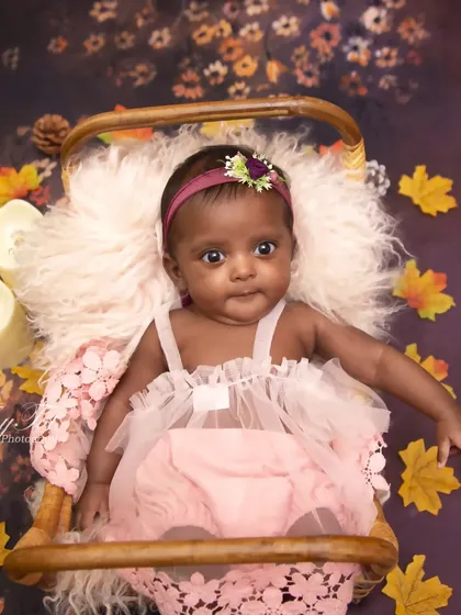 A sweet moment from an autumn-themed sitter session. The baby, dressed in pink, looks directly at the camera, surrounded by fall leaves and candles.