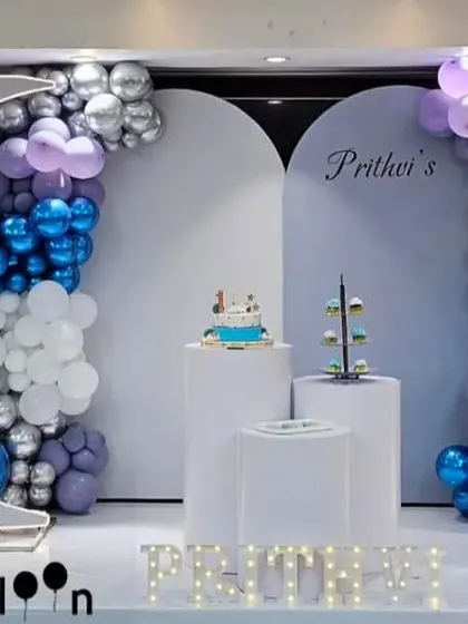 A celestial 'Twinkle Twinkle Little Star' theme for a first birthday. This elegant setup features a large moon prop, balloon arches in purple, blue, and silver, and a light-up number '1'.