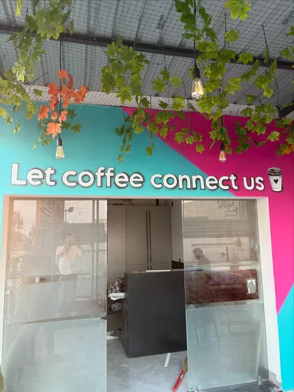 The entrance to the cafe, featuring the acrylic quote "Let coffee connect us" set against a colorful, geometric background.