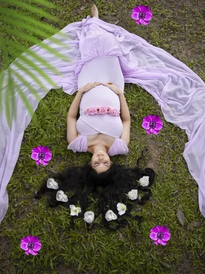 An artistic shot from a gown maternity session. Her hair is styled with soft curls and decorated with white flowers, and the makeup is kept soft and radiant to highlight her pregnancy glow from every angle.