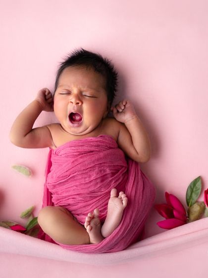 A sleepy yawn from a three-week-old baby, wrapped in a vibrant pink swaddle and surrounded by tulips. A perfect, unscripted moment of newborn life.