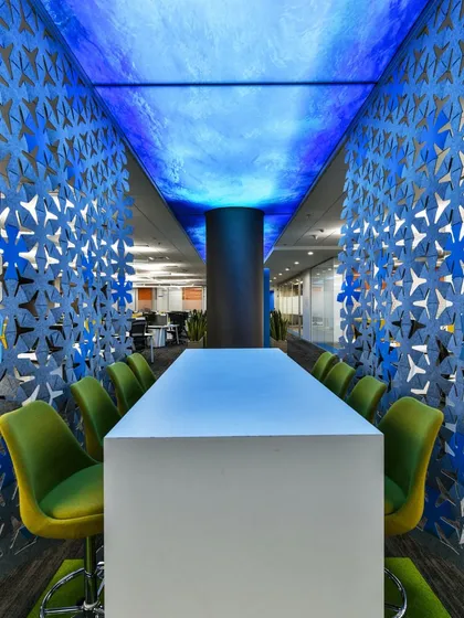 A high-top collaboration table surrounded by a striking blue laser-cut felt screen. The ceiling above features a backlit blue graphic, creating a dramatic and immersive experience.