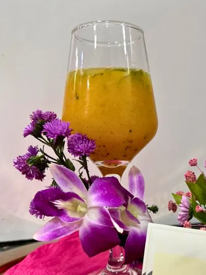 A rich, pulpy mango drink garnished with purple flowers. The vibrant colours and fresh garnish make this a visually stunning beverage option.