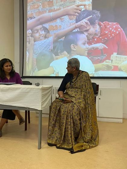 In conversation with a faculty member during my presentation. The image on the screen behind us, showing hands on community work, underscores my belief that architecture has a profound social role.