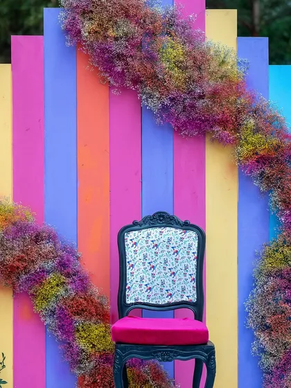 A quirky and colorful photo-op chair, framed by an arc of rainbow-colored baby's breath, perfect for guest pictures.