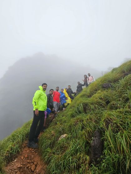 A group of trekkers navigating a narrow, misty trail on the steep slopes of Kurinjal peak. The wild air and rolling meadows make for an unforgettable experience.