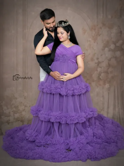 A regal studio portrait of a couple, with the mother-to-be in a purple ruffled gown and crown.