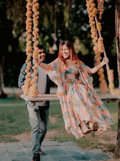A joyful moment of a man pushing his partner on a rustic wooden swing decorated with marigold flowers. This setup is perfect for capturing playful and traditional pre-wedding photos.