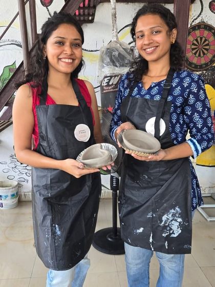 Two friends proudly hold up the simple, elegant bowls they made on the pottery wheel. Even unpainted, the handmade quality gives them a special charm.