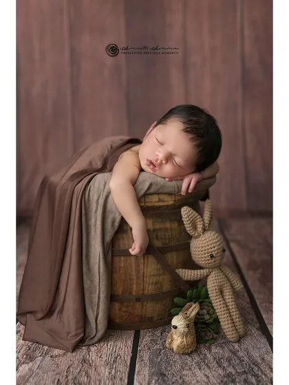 A full view of the rustic bucket pose, complete with a sleepy baby, a knit bunny, and a beautiful wood-textured backdrop.