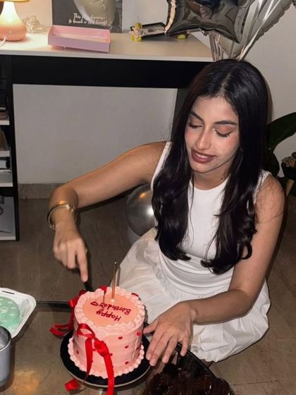 A client celebrating her birthday, cutting into her custom pink and red ribbon cake. The cake perfectly complements the happy and intimate atmosphere of her celebration.