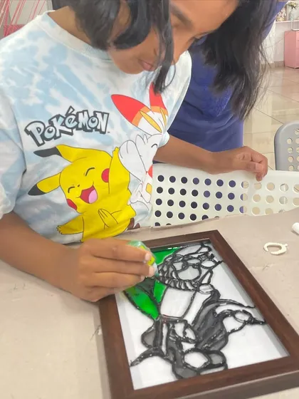 A young artist works on a glass painting, learning how to use special paints to create a stained-glass effect.