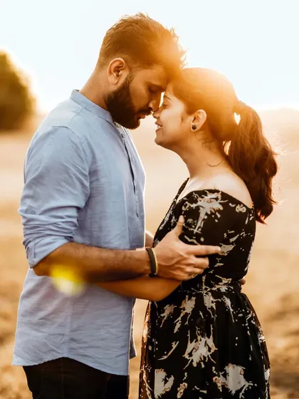 An intimate pre-wedding photo capturing a couple's close embrace against a golden, sunlit field.