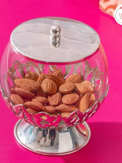 A classic silver and glass dry fruit jar, filled with almonds. This timeless piece makes for a perfect wedding or housewarming gift.