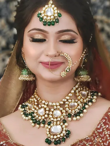 A close-up of a bride wearing a Kundan set with large, heart-shaped stones and green bead drops. A lovely and romantic choice.